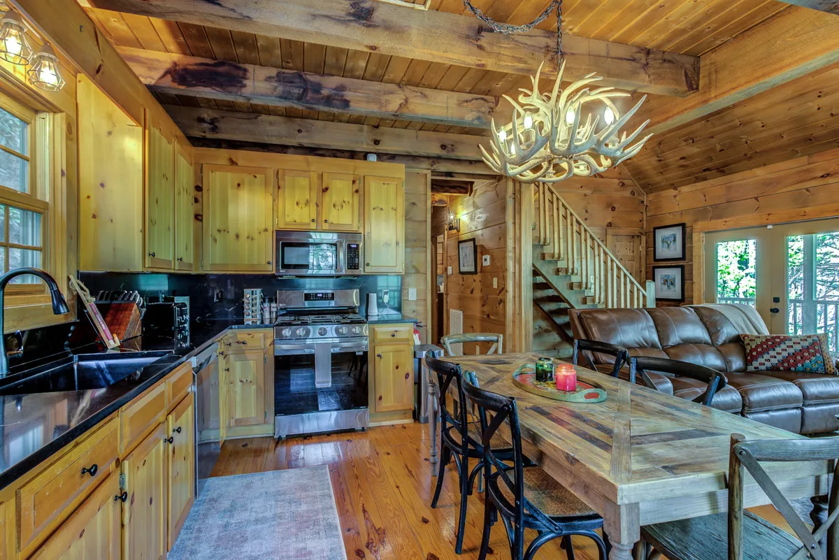 A cohesive view of the living and kitchen areas, showing a leather sofa, dining table, and kitchen cabinetry with modern appliances. The space feels both rustic and up-to-date, with features that support relaxation, entertainment, and meal preparation—all within easy reach for group interaction.