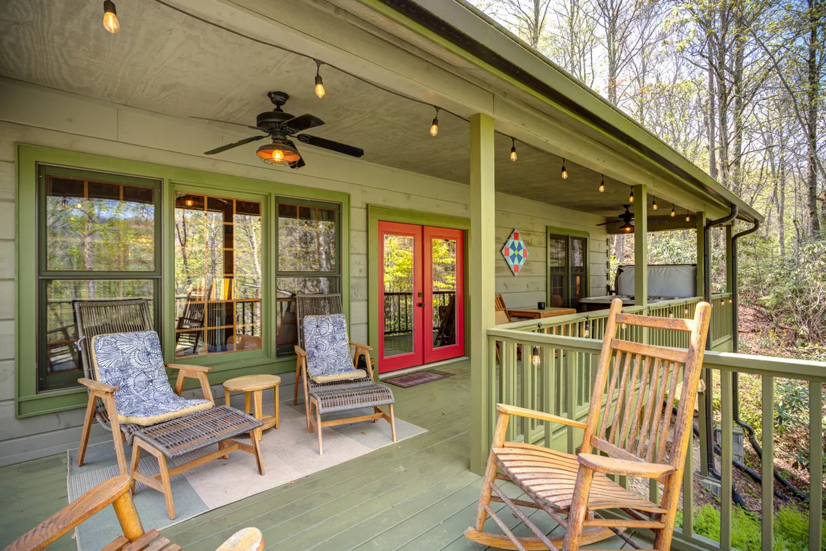 This exterior image features the cabin’s colorful front door, inviting rocking chairs on the porch, and warm hanging lights. The setting hints at a welcoming spot for groups to gather outdoors, whether for quiet morning coffees or lively evenings under the stars.