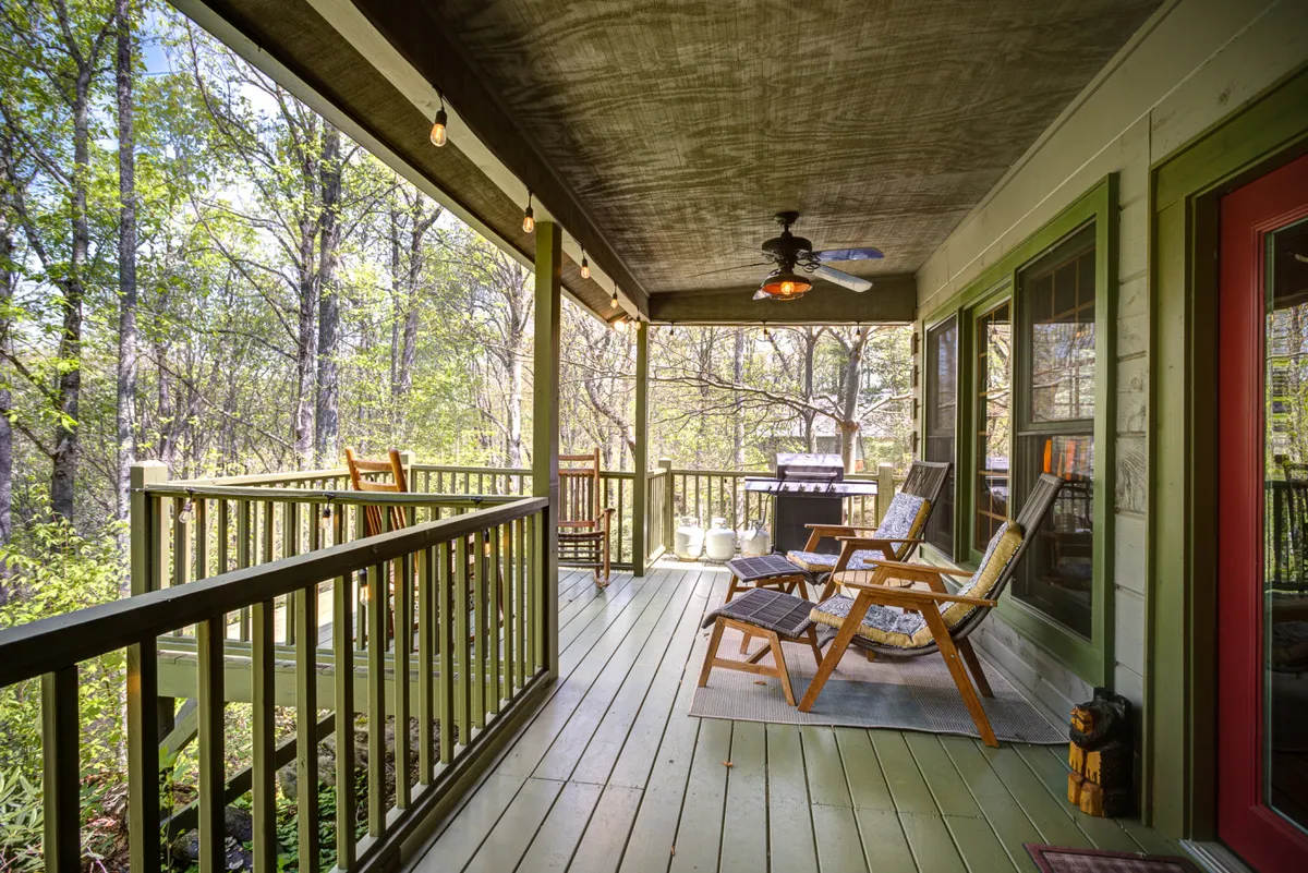 This exterior shot features reclining chairs, a classic wooden rocking chair, and a gas grill on a deck overlooking dense greenery. The setup invites both relaxation and alfresco dining, with the grill ready for summer barbecues.