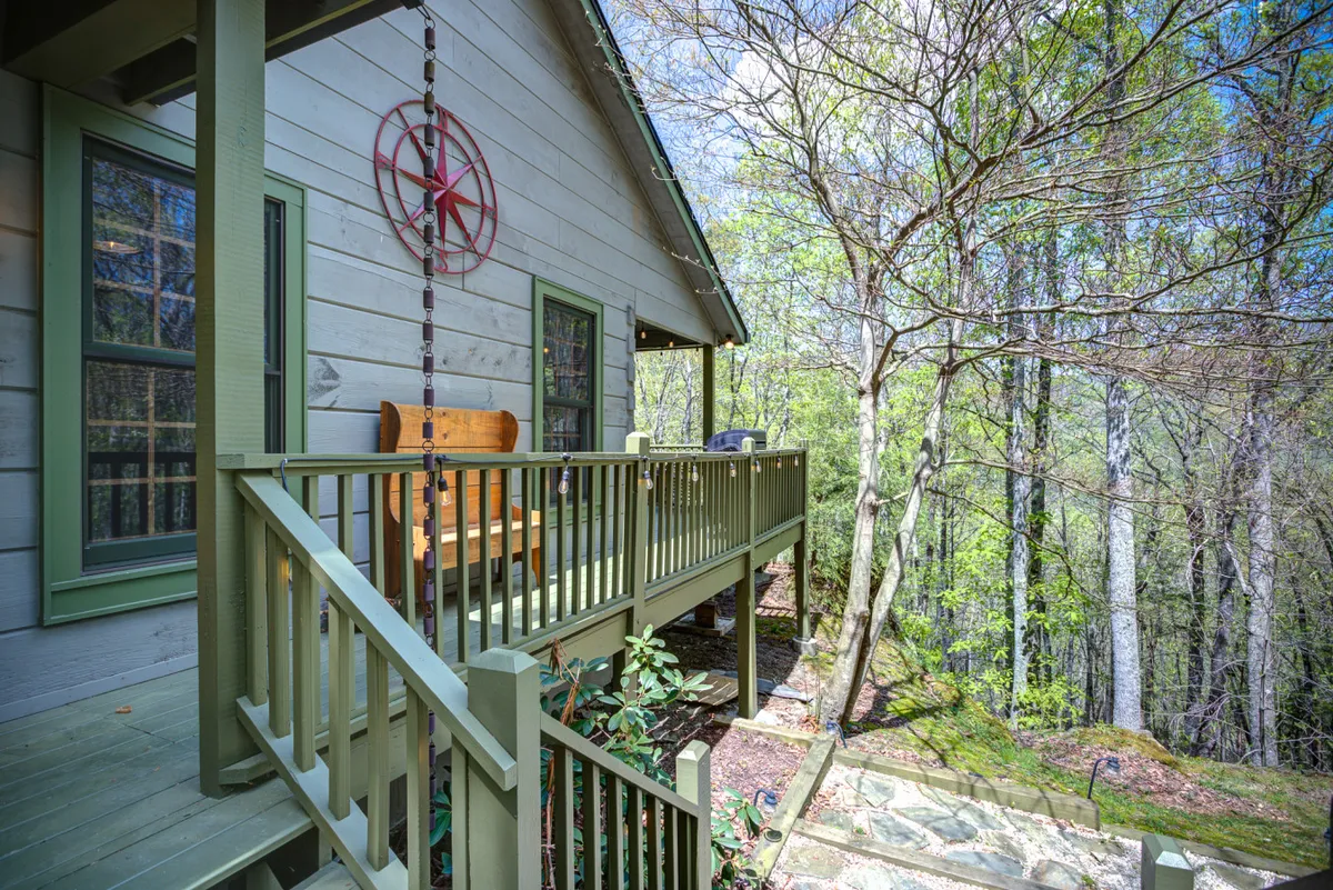 A tranquil porch scene featuring a wooden bench, a star decoration on the wall, and trees in the background. The setting is peaceful, inviting guests to watch wildlife or stargaze together as a family.