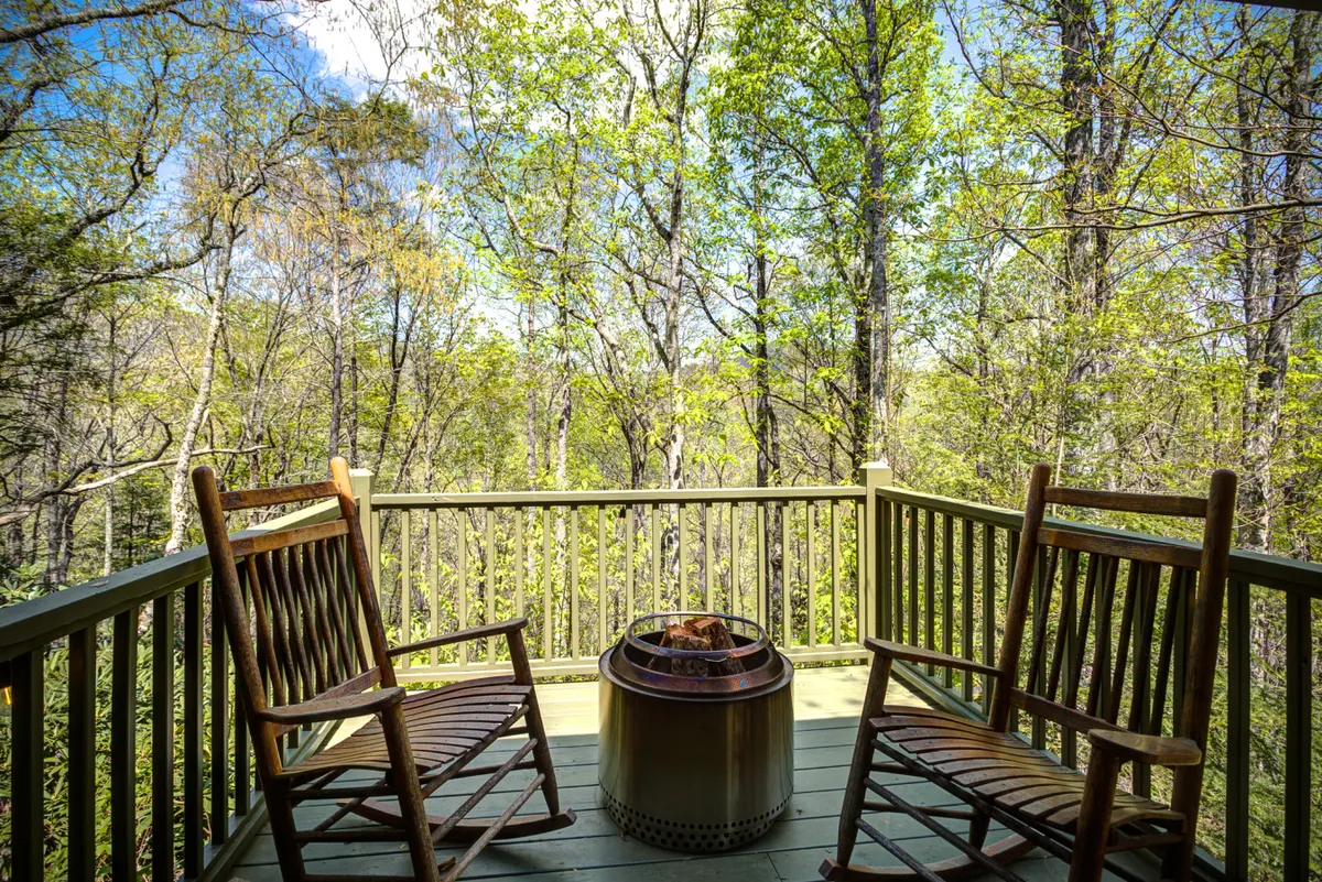 This peaceful outdoor scene highlights rocking chairs gathered around a fire pit, set amidst tall trees. The area is ideal for evening gatherings, storytelling, and enjoying s’mores under the stars.
