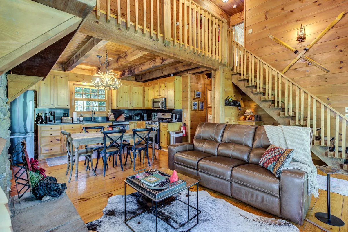 A broad view of the open-concept kitchen and dining area, featuring a leather couch, kitchen area with cabinets, a dining table, and a staircase. The layout invites interaction and highlights how the kitchen and dining spaces flow together, perfect for group activities and shared meals.