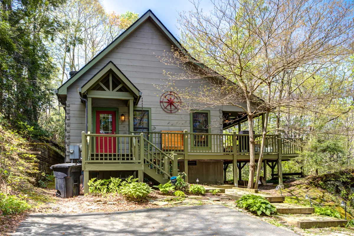 A welcoming exterior view of the cabin's front porch with a distinctive red door and decorative wheel, offering inviting spaces for morning coffee or evening relaxation. The porch exudes charm, with a natural setting that hints at the local vineyard ambiance.